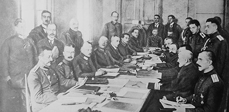 Die deutschen und russischen Delegationen sitzen und stehen um einen Tisch herum bei den Friedensverhandlungen von Brest-Litowsk